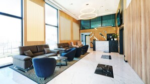 A spacious lobby with a high ceiling, large windows, and a modern reception desk. - WENS Hotel (Mainz)