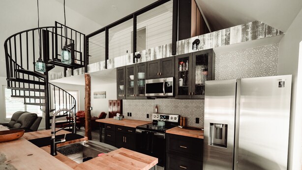 Una cocina moderna con una isla central, electrodomésticos de acero inoxidable y una escalera en espiral.