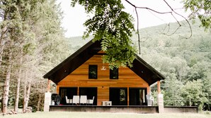 Una cabaña con fachada de madera, ventanas amplias y un porche cubierto con sillas.