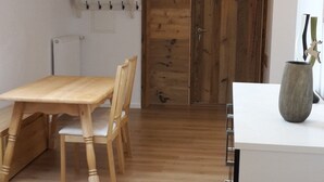 Eine moderne Küche mit Holzboden, einem Esstisch mit Stühlen, einer weißen Arbeitsplatte und einer Holztür.