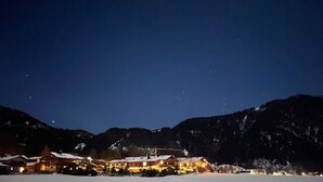 Schneebedeckte Landschaft mit einem beleuchteten Gebäude im Vordergrund, umgeben von Bergen.