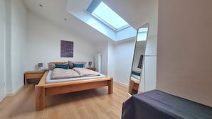 Ein Schlafzimmer mit Dachfenster, einem Bett mit Kissen, einem Nachttisch, einem Spiegel und einer Heizung.