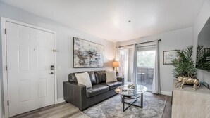 A living room with a dark leather sofa, a glass coffee table, a patterned rug, and a door with a white frame.