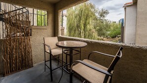 A balcony with a round table and two chairs, a wrought iron gate, and a view of trees and buildings.