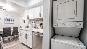 A modern kitchen with white cabinets, a dishwasher, and a built-in washer and dryer.