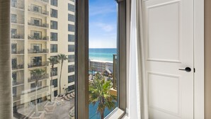 A view from a balcony overlooking a beach and a hotel building. - Origin 0808 - One Bedroom - Sunny Pool Deck & Gulf Views! (Panama City Beach)