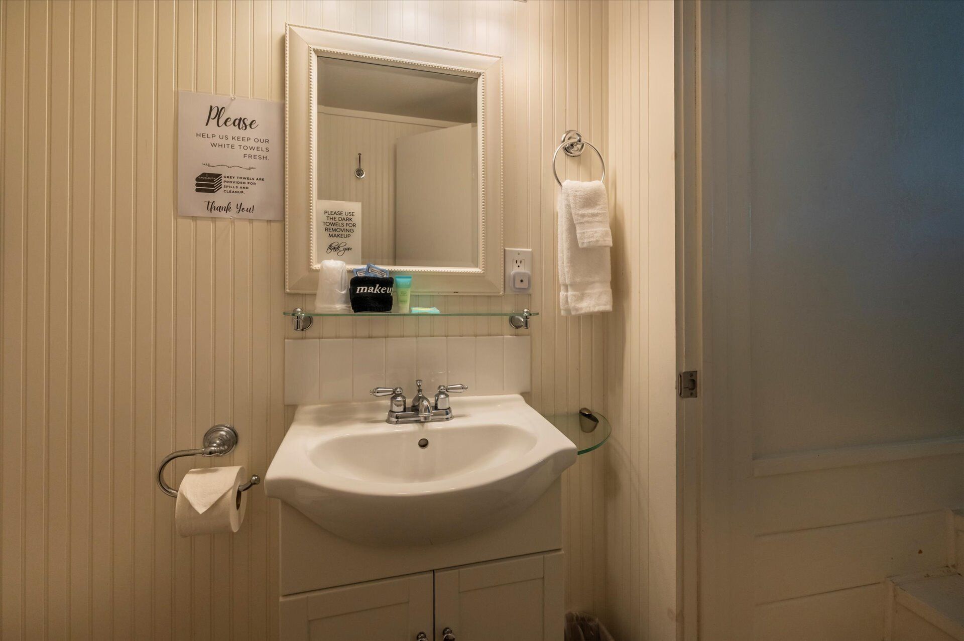 A bathroom with a white sink, mirror, and towel rack. There is a sign above the mirror instructing to use grey towels for cleaning and dark towels for makeup removal.