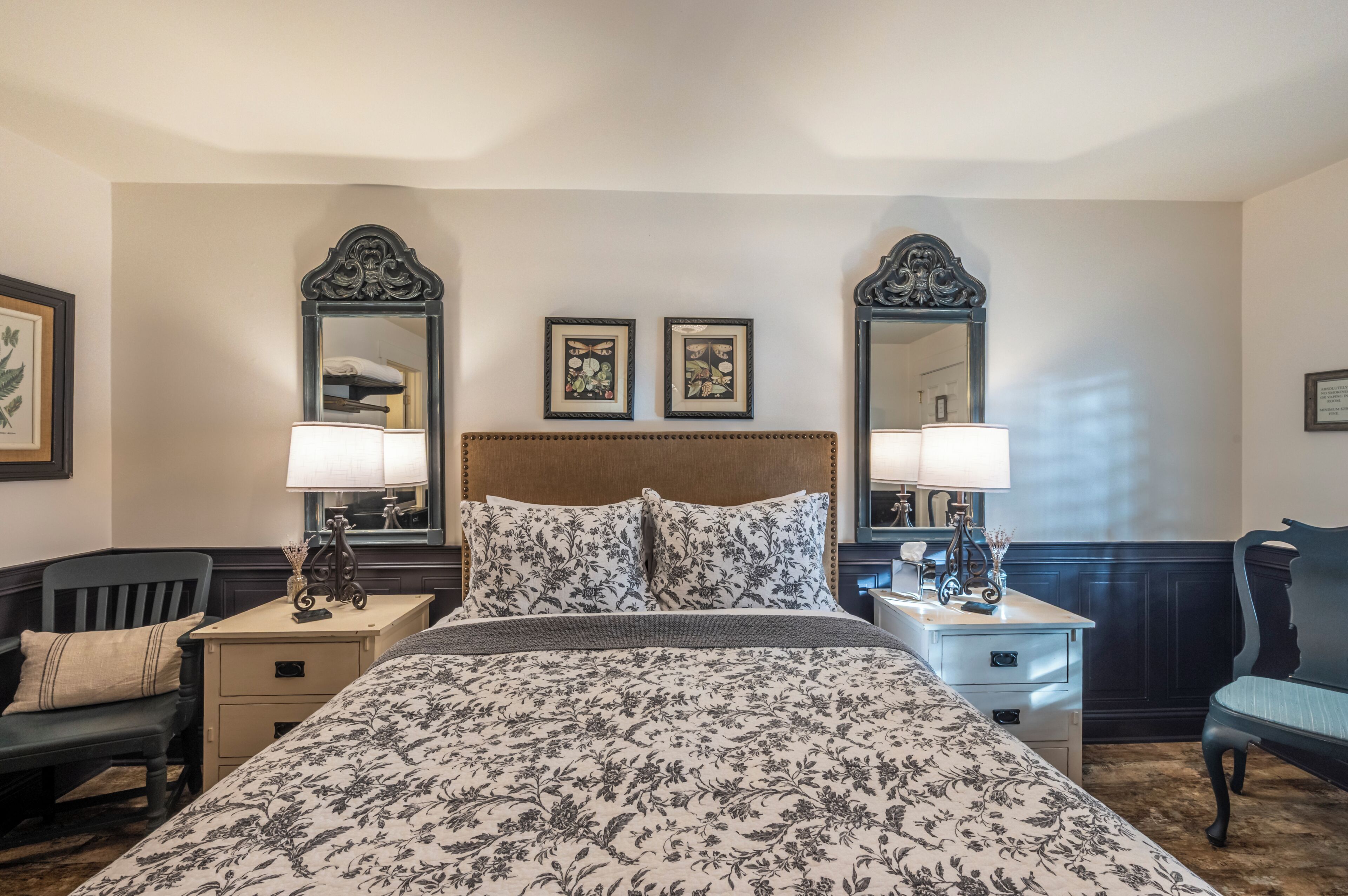 A hotel room with a large bed, two bedside tables, a chair, and two wall-mounted mirrors.