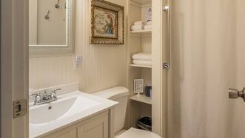 A bathroom with a white sink, toilet, and shower curtain. There is a mirror above the sink and a framed picture on the wall.