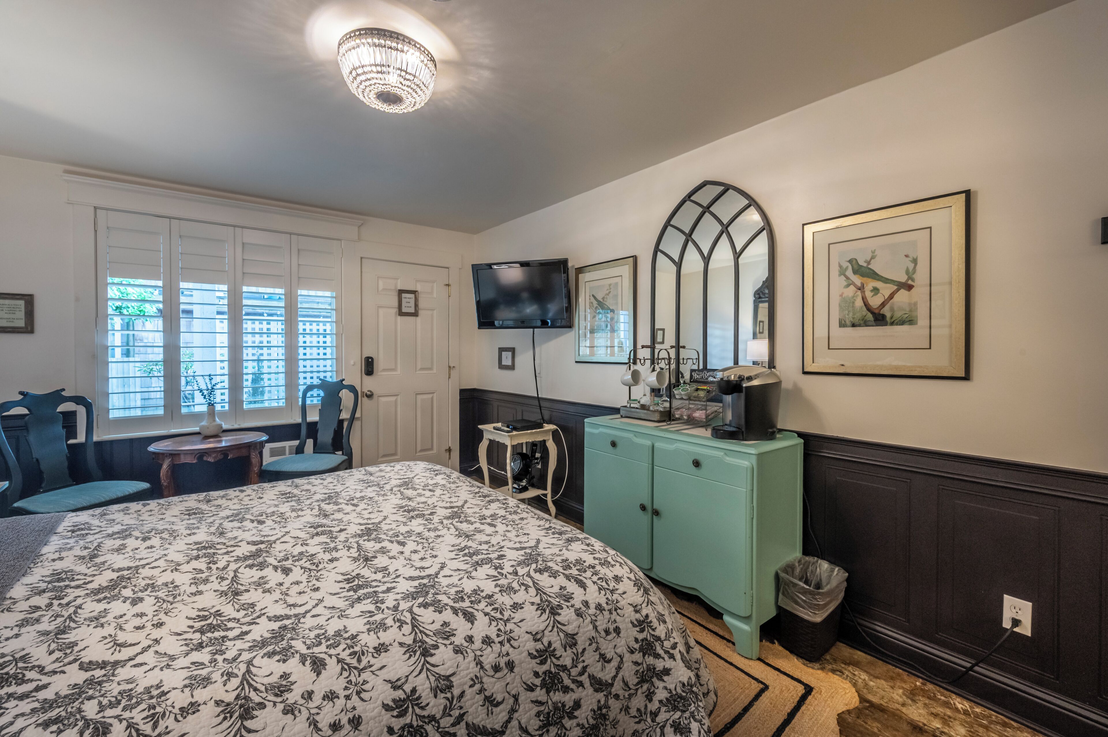 Un dormitorio con cama, televisión, cómoda, espejo y ventana con persianas.