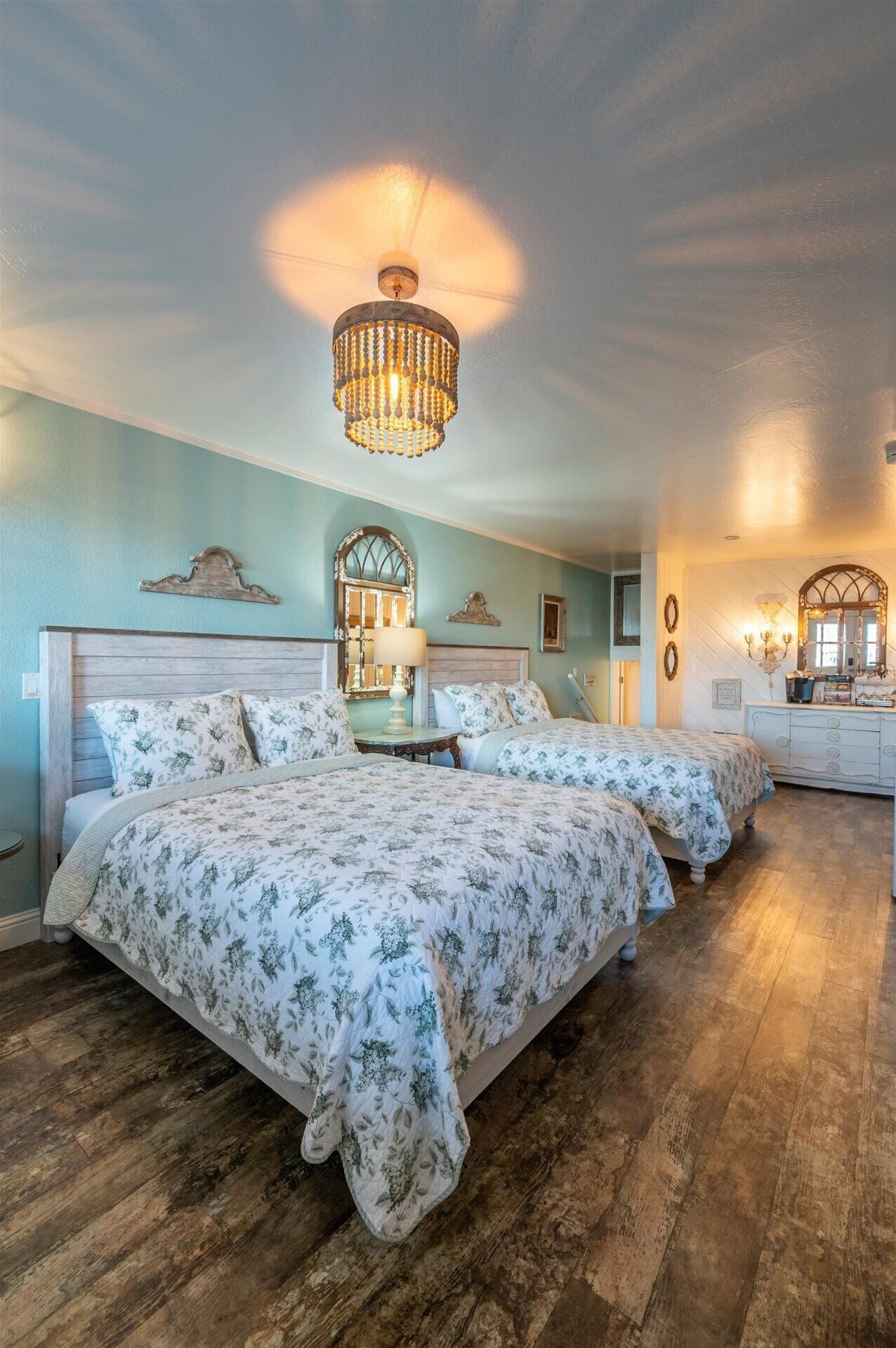 A bedroom with two beds, a chandelier, a dresser, and a mirror.