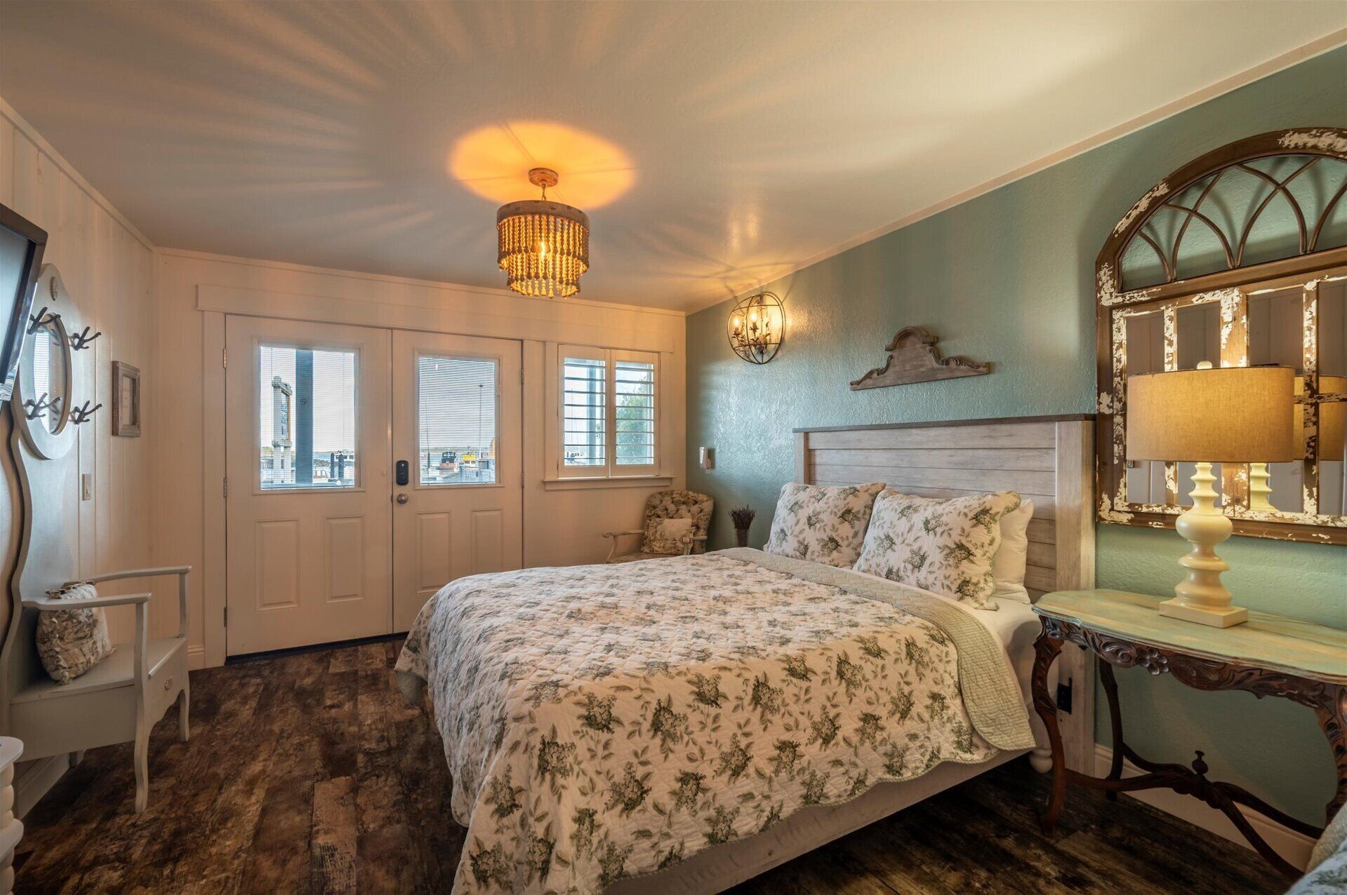 A bedroom with a bed, a nightstand, a lamp, a mirror, and a window with blinds.