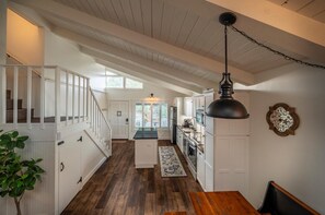 A spacious kitchen with white cabinets, a wooden dining table, and a hanging pendant light. - Bandon Marina Inn (Bandon)