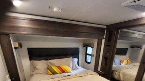 Ein Schlafzimmer mit einem großen Bett, einem Kopfteil, einem Nachttisch und einem Fenster.