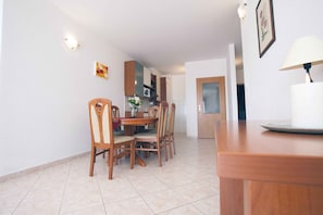 Un coin repas avec une table et des chaises en bois, une cuisine à l’arrière-plan et une lampe sur une table d’appoint.