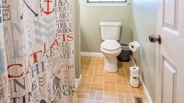 Une salle de bain avec un rideau de douche orné de motifs textuels, des toilettes, une fenêtre donnant sur un paysage et une porte.