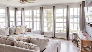 Une pièce spacieuse avec une grande fenêtre, un ventilateur de plafond et une table en bois.