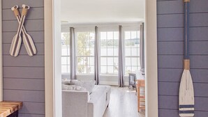 Une pièce avec un plancher en bois, un canapé gris, une table en bois et une vue sur l’extérieur, visible à travers une porte.