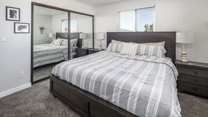 Une chambre à coucher avec un grand lit, une table de chevet, une commode, un miroir et une fenêtre avec des stores.