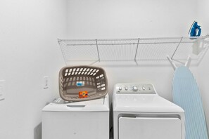 A laundry area with a washing machine, a dryer, a hanging rack, and a basket.