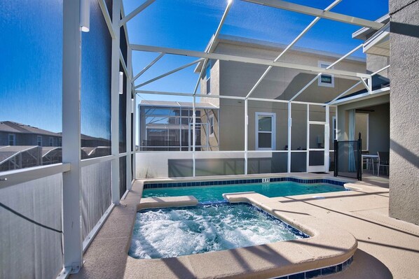 A rooftop pool with a hot tub, surrounded by a glass enclosure, and a clear view of the sky.
