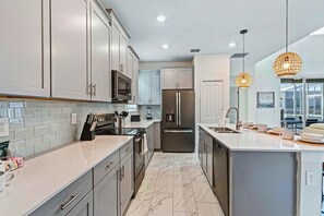 A modern kitchen with stainless steel appliances, white cabinetry, and a marble floor. - Pool, Themed Rooms & Man Cave! 5BR Oasis (Kissimmee)
