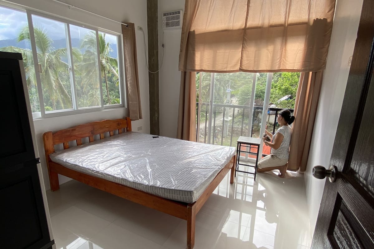 Een slaapkamer met een houten bed, een groot raam en uitzicht op palmbomen.