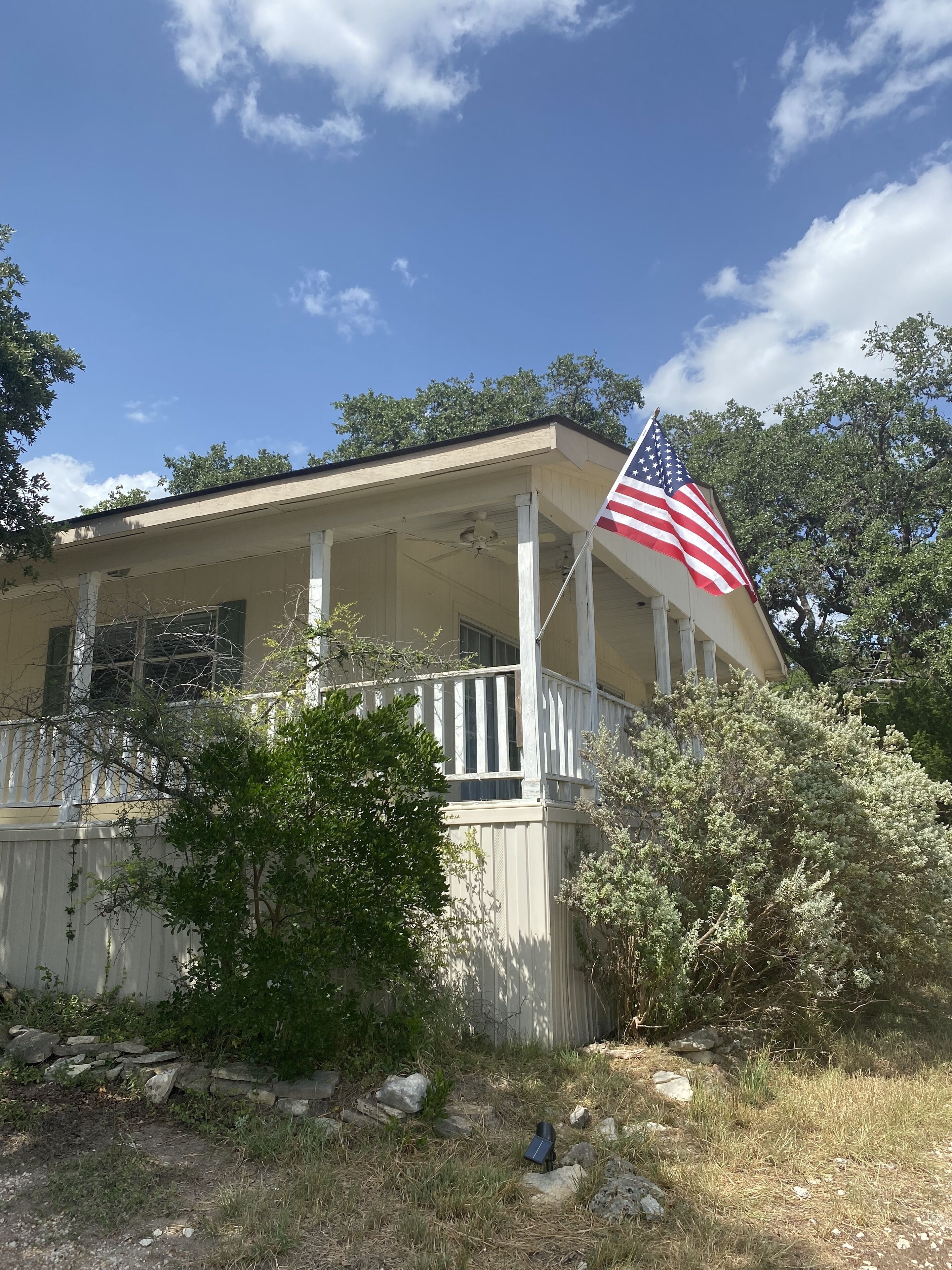 A house with a porch, an American flag, and surrounding greenery.