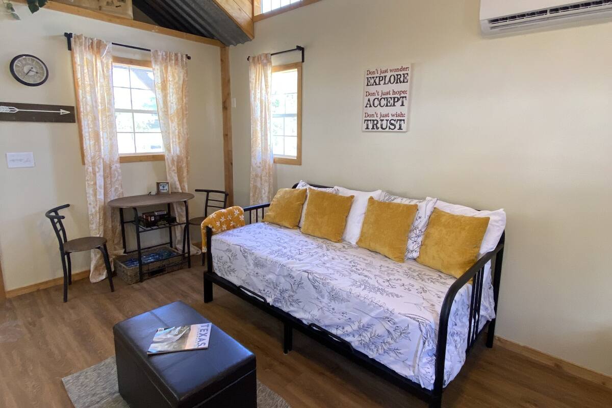 A cozy room with a bed, a small table, and a chair. There is a wall clock and a sign with motivational words.