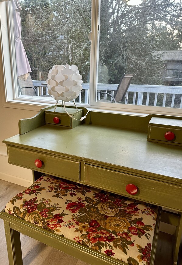 A green wooden desk with two drawers and a floral-patterned bench.
