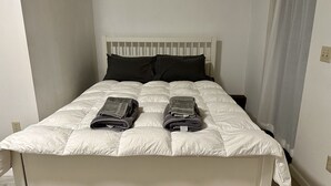 Ein Einzelbett mit weißem Kopfteil, zwei Kissen, einer zusammengeklappten Decke und einem Handtuch.