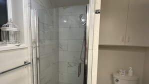 Ein Badezimmer mit einer Glaskabine zur Dusche, einer Toilette und einem Boden aus Marmorfliesen.