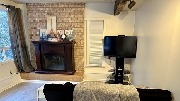 Ein Wohnzimmer mit Kamin, Fernseher, Holztisch und schwarzem Sessel.