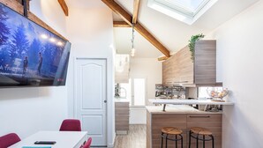 A modern kitchen with wooden cabinets, a bar area, and a dining space with a TV displaying a movie.