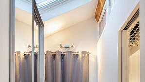 A narrow hallway with a skylight, a wooden floor, and a door leading to a room with a ladder.