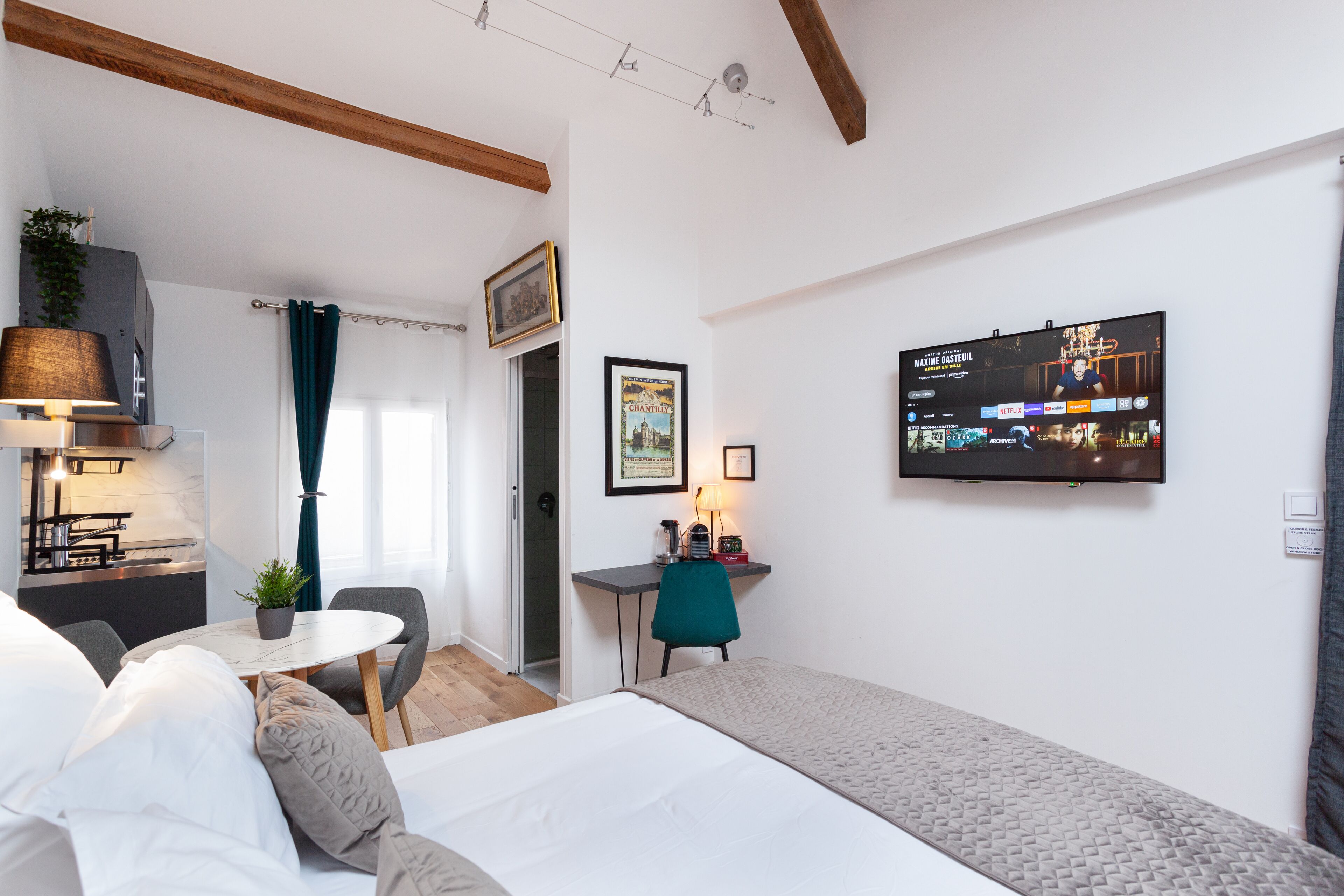A modern hotel room with a bed, a desk, a chair, a TV, and a small table with a plant.