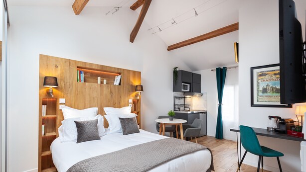 A modern hotel room with a large bed, a desk, and a kitchenette.