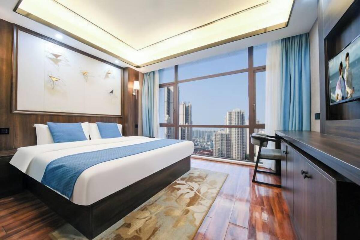 Une chambre d’hôtel moderne, dotée d’un grand lit, d’un bureau et offrant une vue sur le paysage urbain.