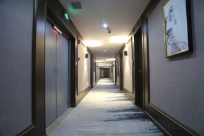 Corridoio d'albergo con porte su entrambi i lati, pavimento rivestito di moquette e un quadro appeso alla parete destra.