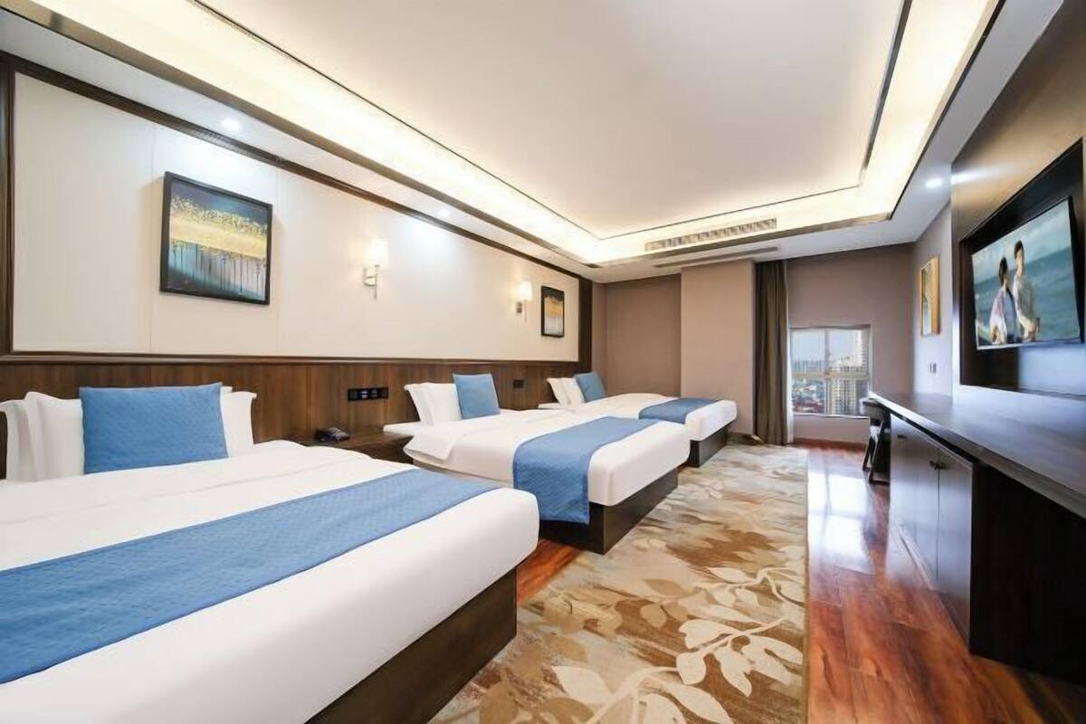 Une chambre d’hôtel avec trois lits, une télévision et une grande fenêtre.