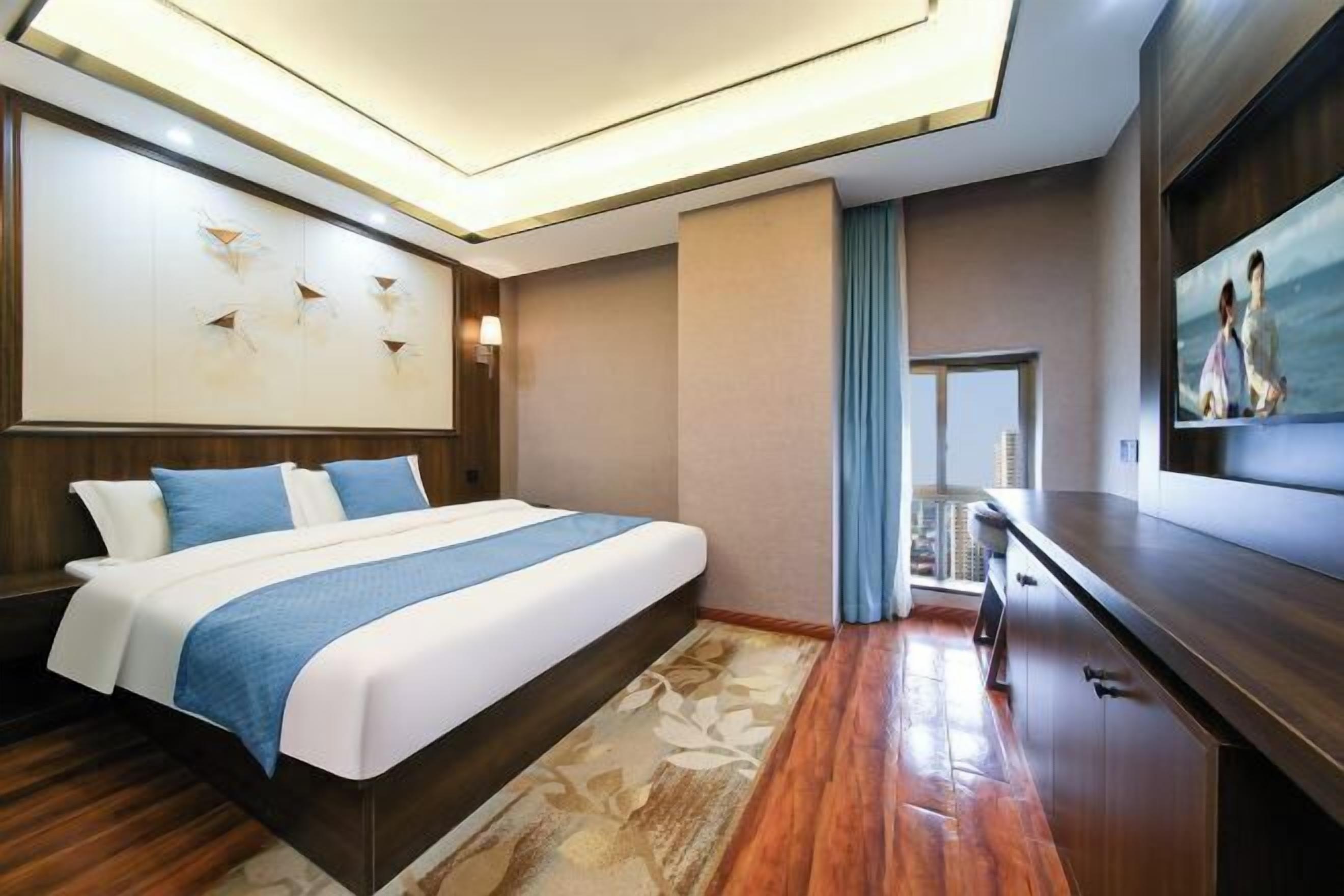 A modern hotel room with a large bed, a flat-screen TV, a wooden floor, and a view of the cityscape.