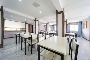 Una sala conferenze d'hotel con diversi tavoli e sedie, un angolo cottura e ampie finestre.