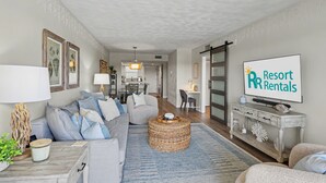 A living room with a sofa, a round wicker coffee table, a TV, and a sign for 'Resort Rentals'.
