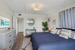A bedroom with a bed, dresser, vanity, mirror, and a sign for 'Resort Rentals'.