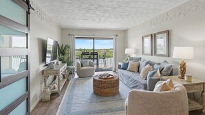 A living room with a sofa, a coffee table, a TV, and a view through a large window.