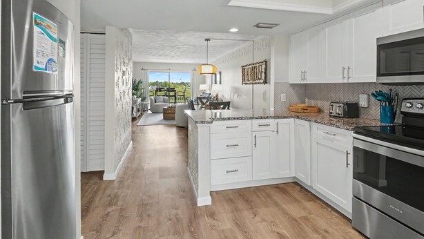 A modern kitchen with white cabinetry, stainless steel appliances, and a herringbone-patterned backsplash.