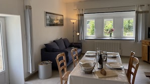 Un coin repas avec une table dressée pour deux personnes, un canapé et une fenêtre avec des rideaux.