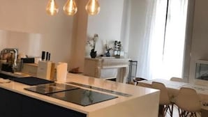 A modern kitchen with a central island, pendant lights, and a dining area with a table and chairs. - Le Marais Historique rue des Rosiers (Paris)