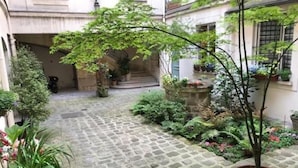 A courtyard with cobblestone flooring, potted plants, and a staircase leading to an upper level. - Le Marais Historique rue des Rosiers (Paris)