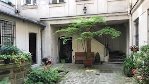 A courtyard with a cobblestone path, a wooden bench, and potted plants. - Le Marais Historique rue des Rosiers (Paris)